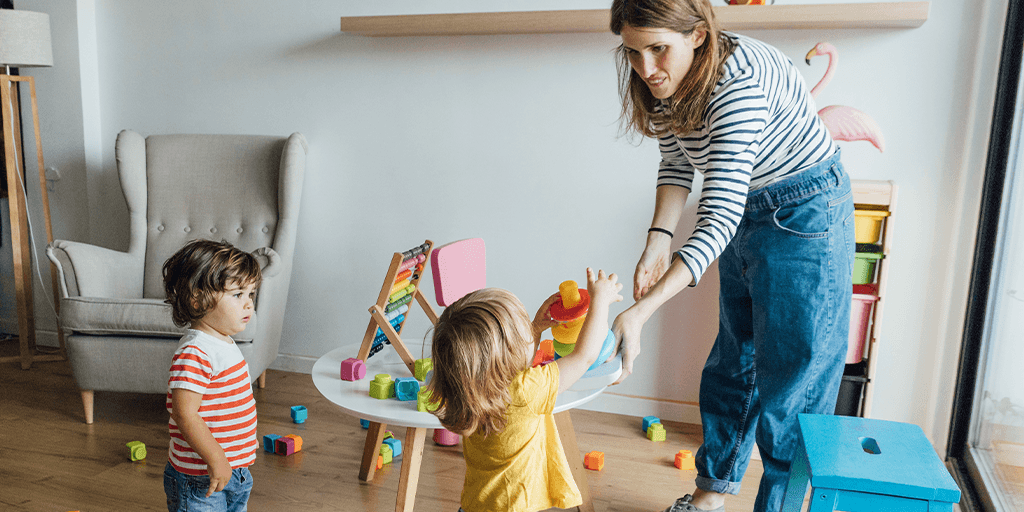 A woman helps two young children in child care setting