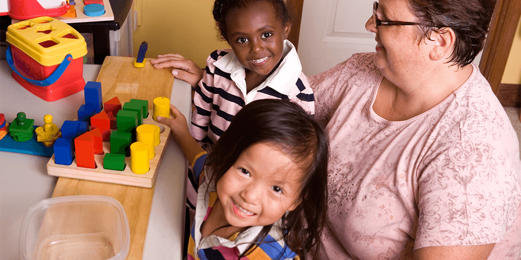 A woman sits with two young children in a child care setting