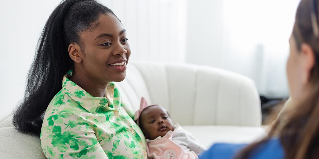 a young woman holds her baby and talks to a nurse