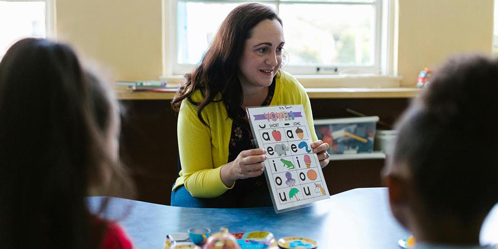 a teacher shows her students a chart with vowels on it